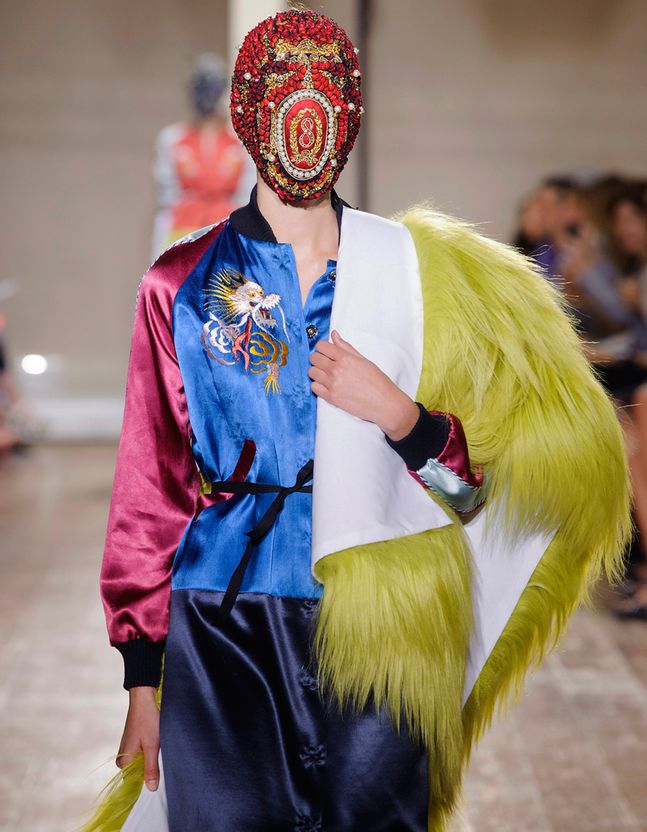 Mannequin habillé de divers couleur qui porte un masque rouge avec des motifs dessus